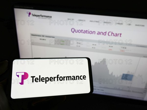 Stuttgart, Germany, 05-21-2022: Person holding mobile phone with logo of French company Teleperformance SE on screen in front of business web page. Focus on phone display