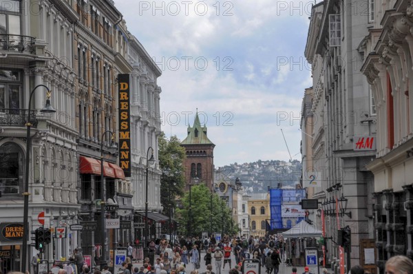 Busy shopping street with several shops, in the background a hilly panorama and cloudy sky, oslo, norway