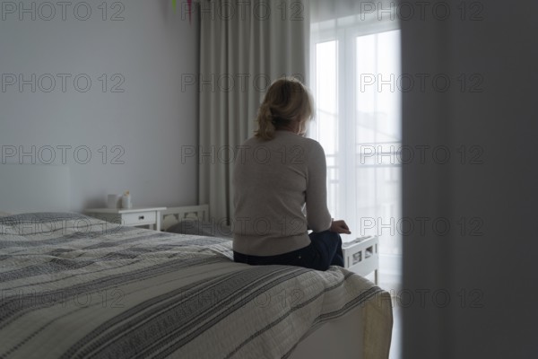 Mature woman sitting alone in the room, sad depressed person. Back view. mental health problemageing population.