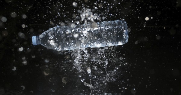 Bottle of Water falling on Water against Black Background