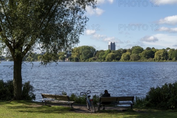 Leisure activities in summer, bicycle and woman on park bench, blue sky, Alster with Hotel Radisson, Hamburg, Germany