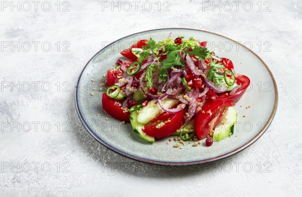 Georgian vegetable salad, cucumbers with tomatoes, greens, walnuts, pomegranate seeds, on a light background, close-up, homemade, no people
