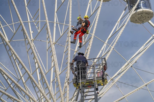 Two climbers and another worker during a rescue operation on the Ferris wheel, fire brigade exercise for gondola rescue, Germany