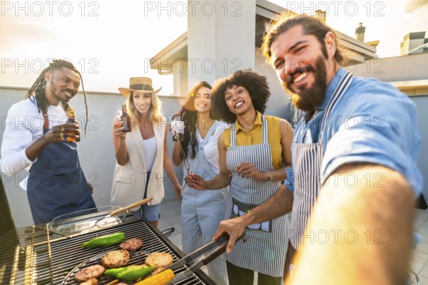 Cheerful friends enjoying rooftop barbecue party, grilling food and beverages and taking a selfie