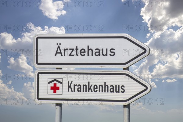 (Photomontage) Directional arrows with the inscription ÄRZTEHAUS and KRANKENHAUS against a blue sky