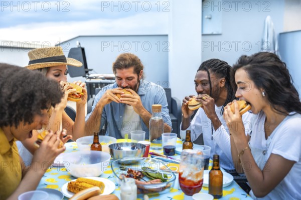 Cheerful multi ethnic friends savoring delicious burgers while enjoying a lively rooftop barbecue party, celebrating summer together