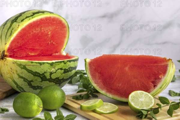 Sliced watermelon with limes and mint leaves on a wooden board