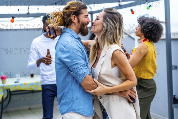 Happy couple embracing and sharing joyful moments with friends while sipping drinks at a lively rooftop party under the city lights