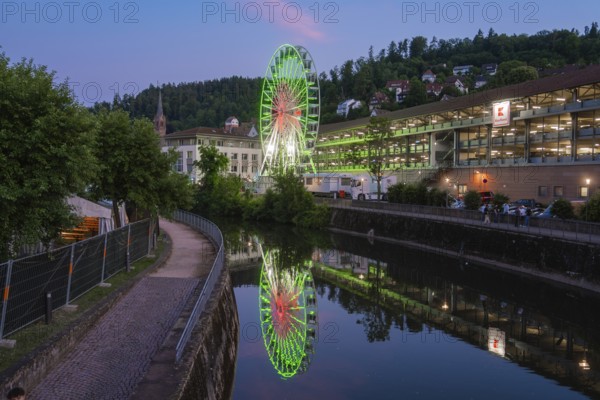 A Ferris wheel shines in blue and green and is reflected in a calm river at night, 950 years of Calw, Germany
