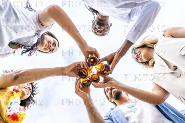 Group of cheerful multi ethnic friends toasting with beer bottles, enjoying a summer beach party together