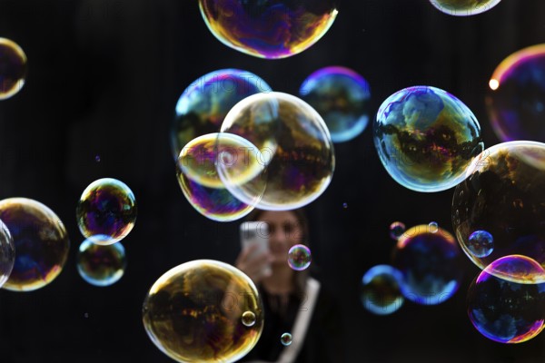 A woman photographs shimmering and floating soap bubbles against a black background, Recklinghausen, North Rhine-Westphalia, Germany