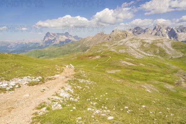 A winding path through green countryside with spectacular mountain panoramas and skies, hike to the Schlehrn, Alpe di Siusi, Dolomites, South Tyrol, Italy