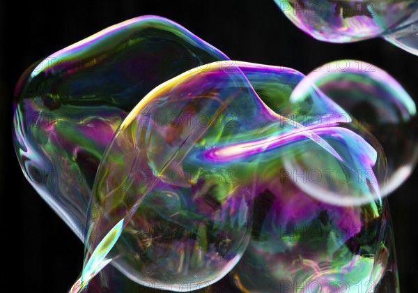 Large, irregular, iridescent soap bubbles in the colours of the rainbow against a black background, Recklinghausen, Germany