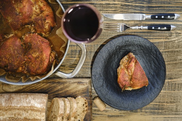 Overhead view of roasted meatin a plate and baking pan served with freshly sliced bread and a glass of red wine