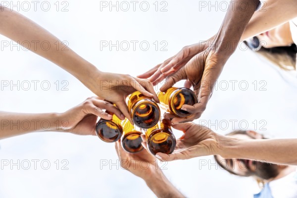 Group of friends toasting with beer bottles against a bright sky, celebrating friendship and enjoying a refreshing moment together