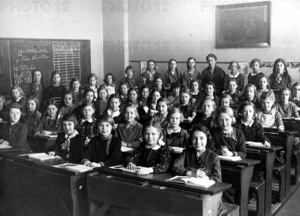 Girls' class school bench, 1920s, A group of schoolgirls sitting on wooden benches in a classroom, Historical photo