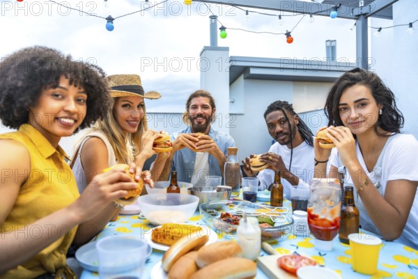 Cheerful multi ethnic friends savoring delicious burgers while enjoying a vibrant rooftop barbecue party with stunning city skyline views