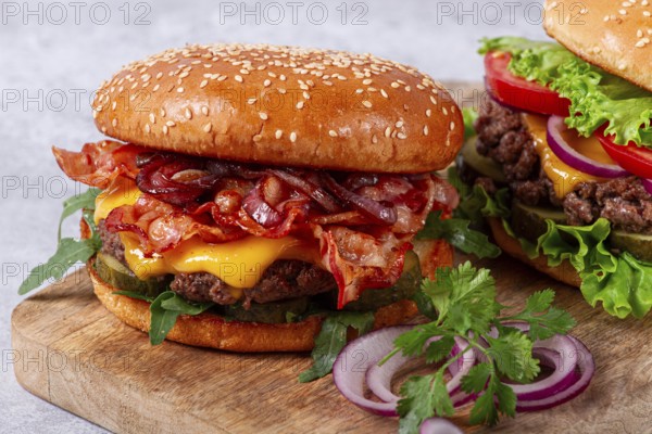 Two burgers with beef patty, fried bacon, cheddar cheese, tomatoes, homemade, no people