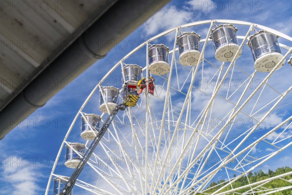 A crane lifts people on a large Ferris wheel up into the blue sky, fire brigade exercise for gondola rescue, Germany