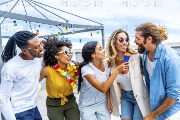 Five cheerful friends singing karaoke, holding a microphone and enjoying a rooftop party during summertime