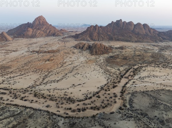 Spitzkoppe (1728 m) - on the left - and Pondok Mountain majestically rise above the surrounding desert plains. At dawn. Aerial view. Drone shot. Damaraland, Namibia