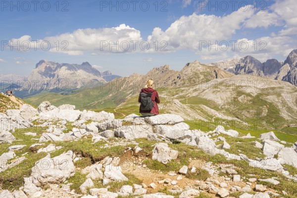 Person sitting on rock with rucksack, mountain panorama and blue sky in the background, hike to Schlehrn, Alpe di Siusi, Dolomites, South Tyrol, Italy