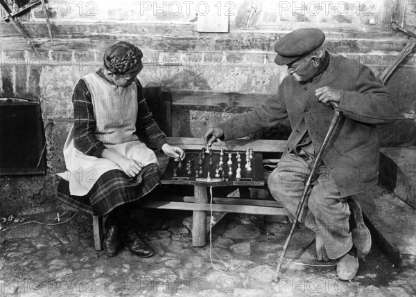 Old man playing chess with girl 1900, Two elderly people playing chess on a bench outdoors, Historical photo