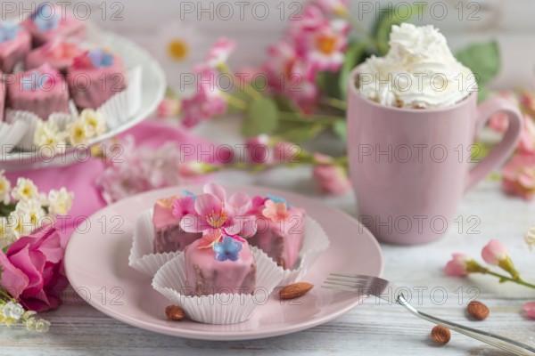 Pink petit fours with flower decoration on a plate next to a cup of coffee with cream