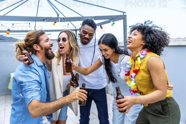 Cheerful multi ethnic friends are toasting with bottles of beer, laughing and having fun at a rooftop party
