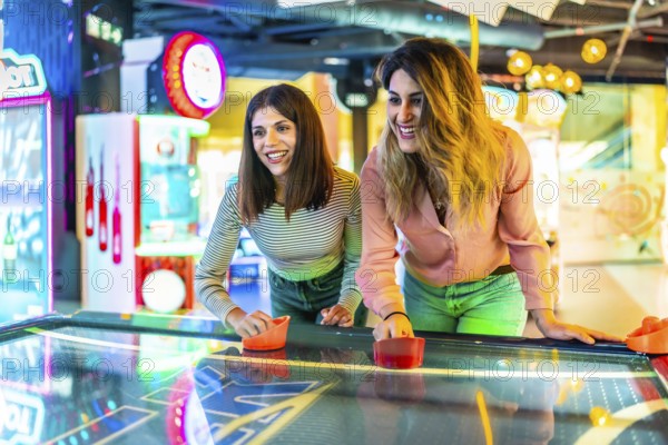 Two young women enjoying a friendly game of air hockey in a vibrant arcade, showcasing fun and entertainment