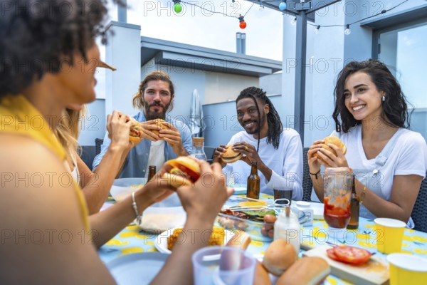 Cheerful multi ethnic friends savoring burgers and drinks while enjoying a lively rooftop barbecue party filled with laughter and connection