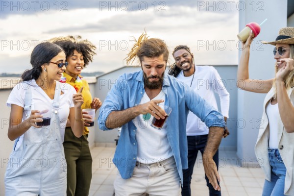 Young people enjoying drinks and dancing joyfully at a vibrant rooftop party, celebrating summer evenings under a stunning sunset