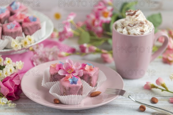 Pink petit fours with flower decoration on a plate next to a cup of coffee with cream