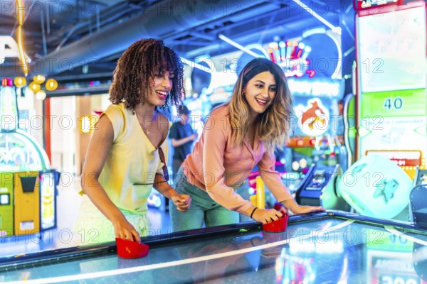 Two young women enjoying a friendly game of air hockey in a vibrant arcade, illuminated by colorful neon lights