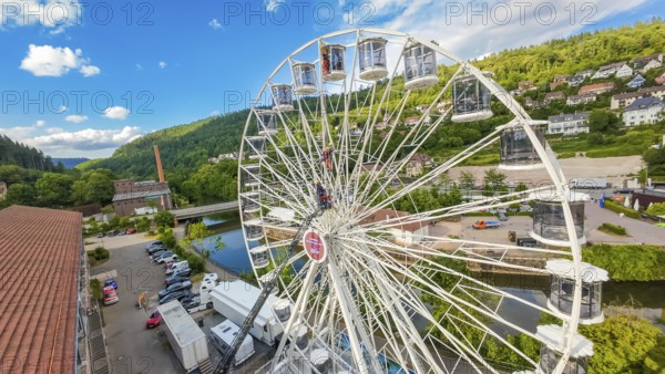 A Ferris wheel with lorries underneath, near a river in a green environment, fire brigade exercise for gondola rescue, Germany