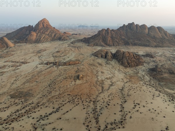Spitzkoppe (1728 m) - on the left - and Pondok Mountain majestically rise above the surrounding desert plains. At dawn. Aerial view. Drone shot. Damaraland, Namibia