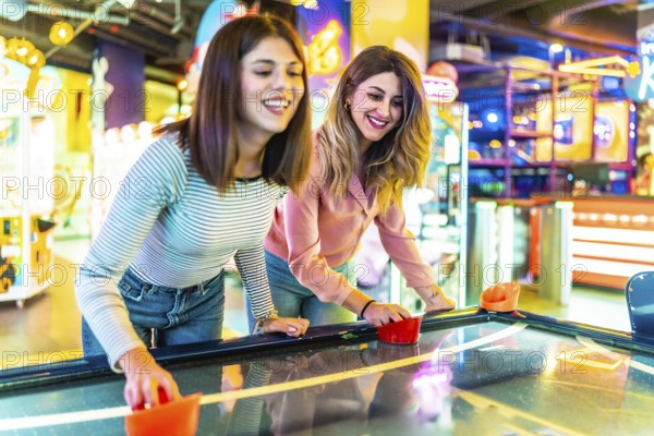Two young women enjoying their free time playing air hockey in a colorful and modern amusement arcade