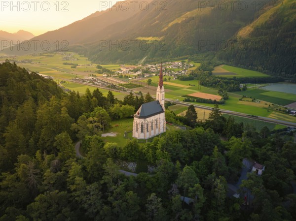 View from a hill with a church over a wide valley at sunset