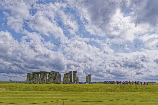 A group of tourists visits Stonehenge. The stone circle, a National Trust, UNESCO World Heritage Site, is a megalithic structure from the Neolithic period and is considered a place of power. The site consists of a ring-shaped earth wall, inside which there are various formations of carved stones grouped around the centre. Amesbury, Wiltshire, South England, Great Britain