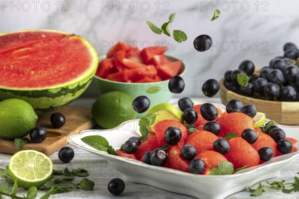 Grapes fall on fruit bowl with watermelon, lime and mint in front of ingredients