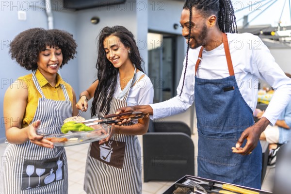 Happy multi ethnic friends preparing grilled vegetables and meat, enjoying barbecue party on the rooftop