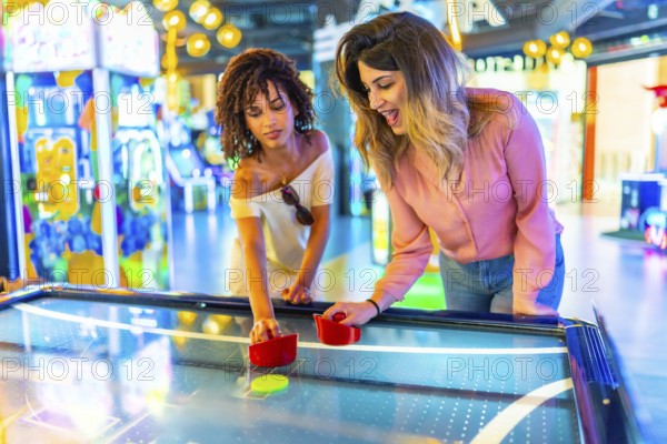 Two young women enjoying a friendly game of air hockey in a vibrant arcade, showcasing the fun and excitement of indoor entertainment