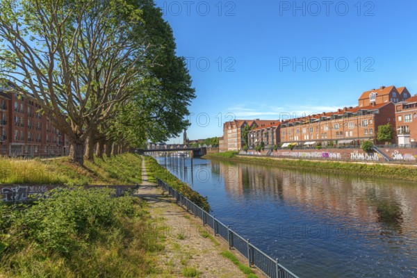 View from Alte Neustadt across the Weser to the Teerhof peninsula, brick architecture, hiking trail, row of trees, water reflection, cultural church St. Staphani, blue sky, Hanseatic City of Bremen, Germany