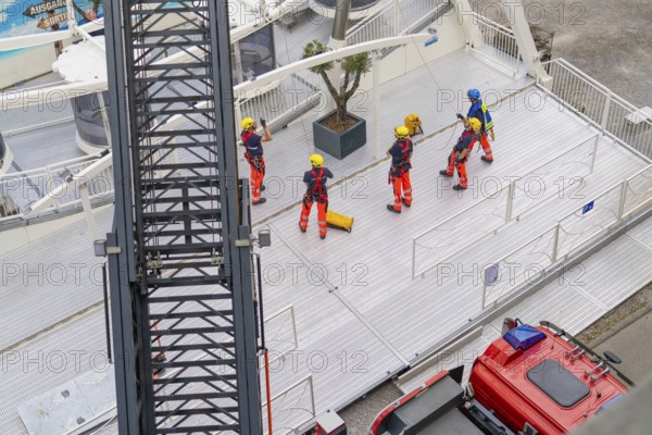 Several firefighters stand on a platform next to a crane jib, fire brigade exercise for gondola rescue, Germany