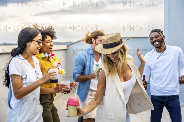 Cheerful multi ethnic friends enjoying cocktails and dancing joyfully at a vibrant rooftop party against a stunning city skyline