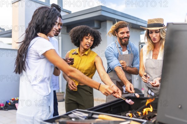 Cheerful friends roasting marshmallows on skewers over a barbecue grill during a rooftop party