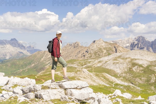 Person standing on rocks, surrounded by a mountain landscape under a blue sky, hike to the Schlehrn, Alpe di Siusi, Dolomites, South Tyrol, Italy