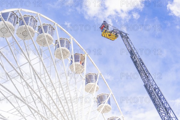 A crane near a Ferris wheel lifts equipment against a cloudy sky, fire brigade exercise for gondola rescue, Germany