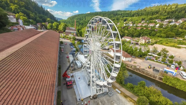 View of a Ferris wheel in a wooded environment with red roofs and blue sky, fire brigade exercise for gondola rescue, Germany