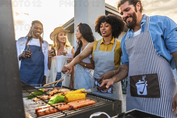 Chefs cooking meat and vegetables on barbecue grill during rooftop party with friends drinking beer at sunset